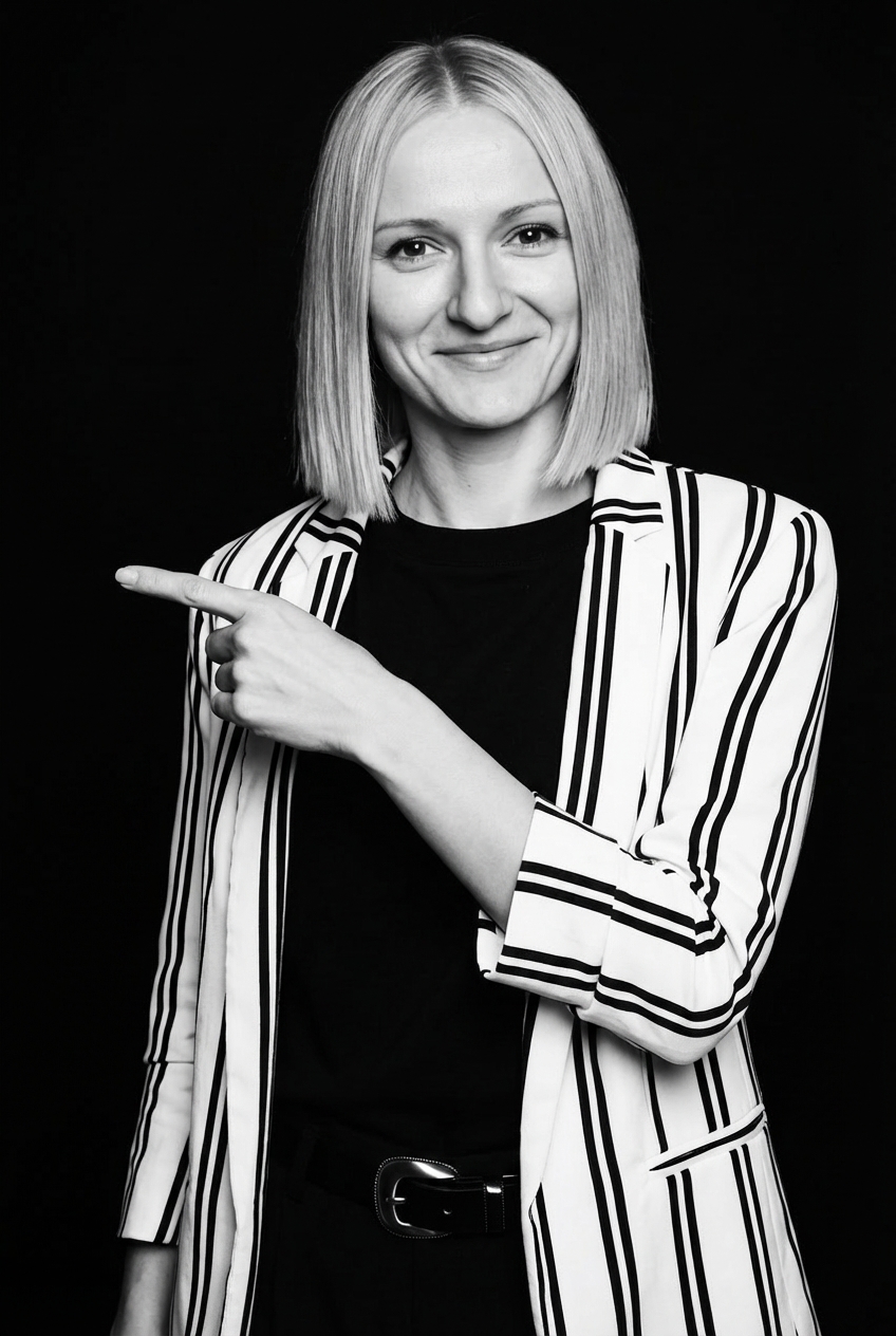 Justyna pointing left with a warm smile in a professional striped blazer